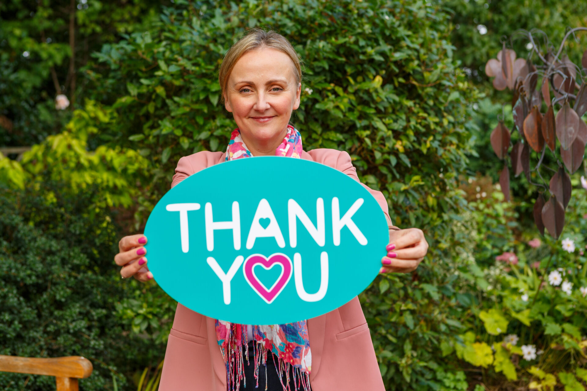 Rachel Street holding up a sign that says 'thank you' standing in the Hospice garden with the memory tree in the background,