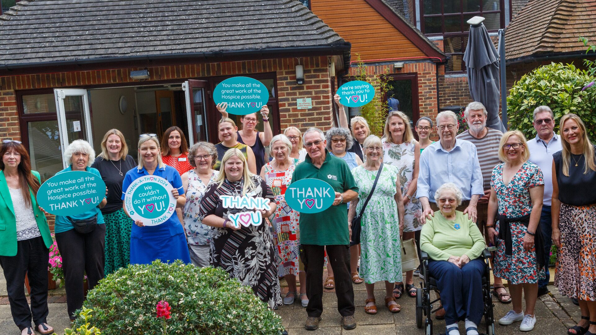 A group of colleagues and volunteers in front of the Hospice holding thank you signs