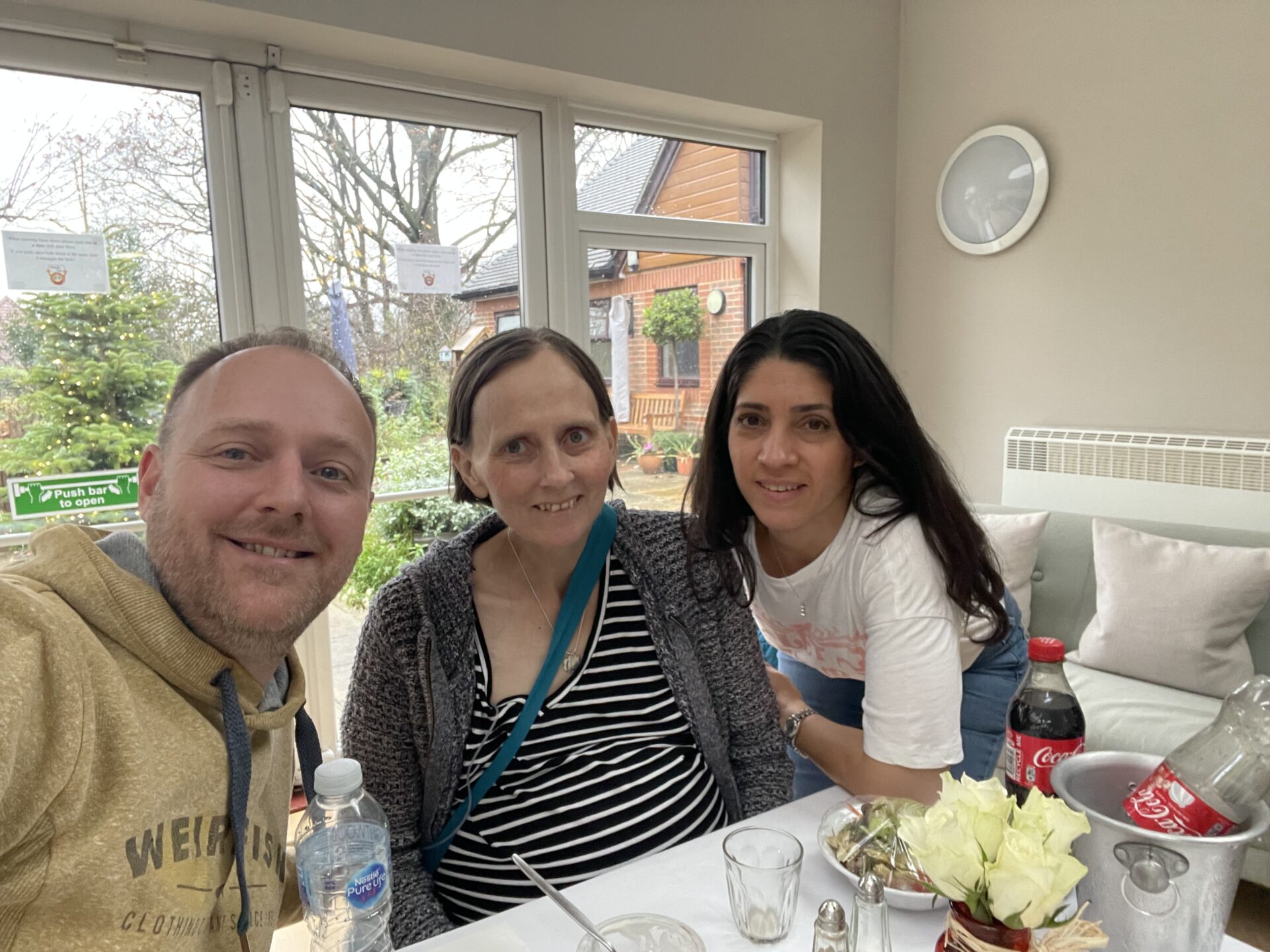 Amelia and Family Two women and a man pose for a selfie with the Hospice garden in the background