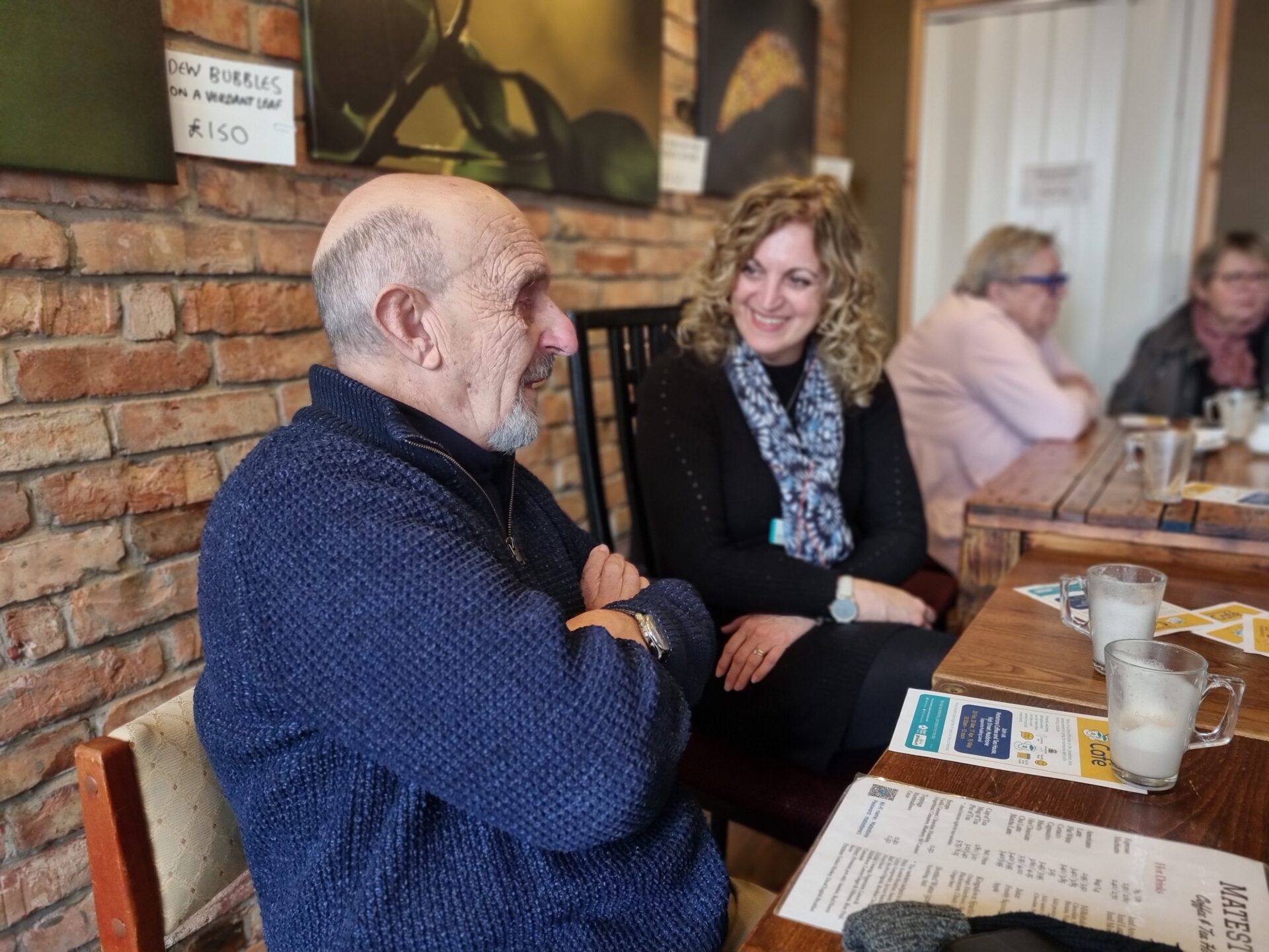 A photograph of a man and a woman chatting round a table over coffee