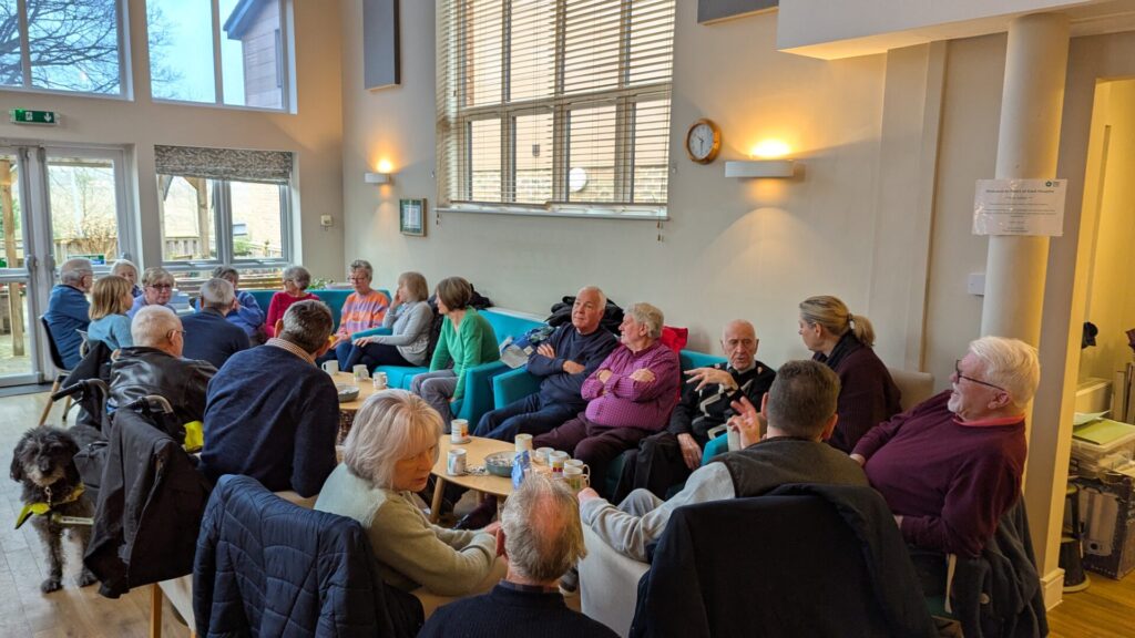 A group view of the Heart of Kent Hospice bereavement drop-in. People sit talking and drinking tea.